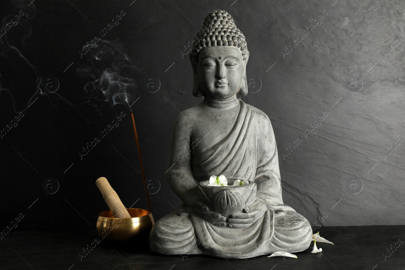 Photo of Buddha statue with petals near singing bowl on black table