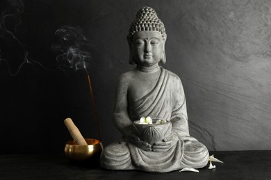 Buddha statue with petals near singing bowl on black table