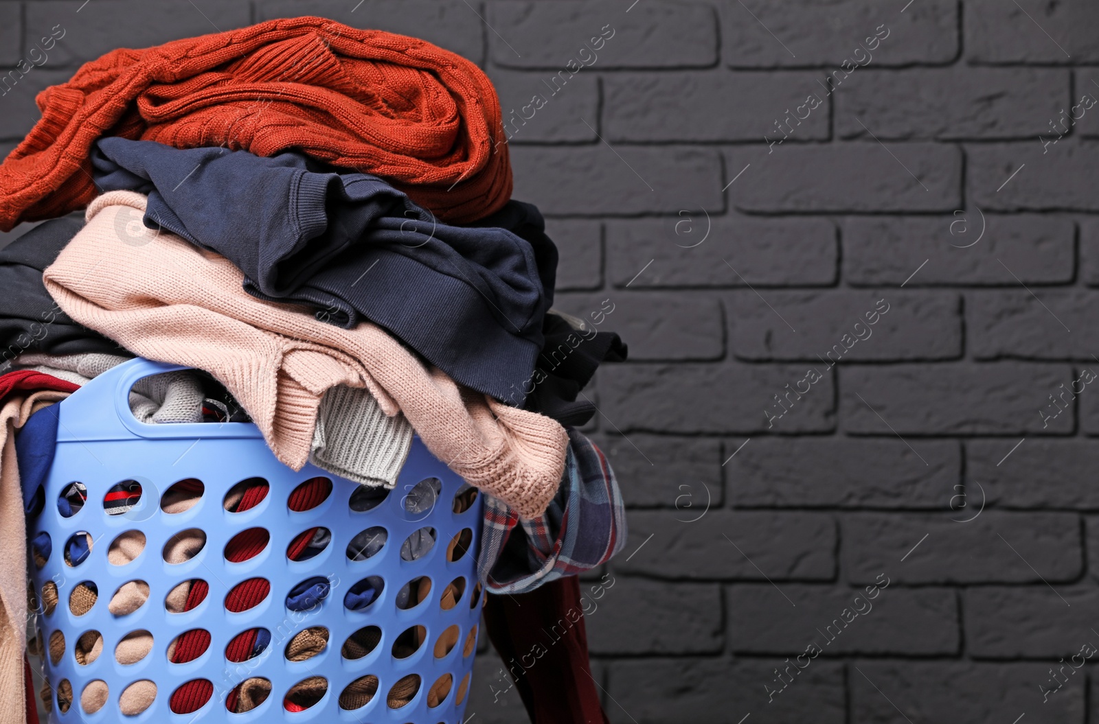 Photo of Laundry basket with clothes near black brick wall. Space for text