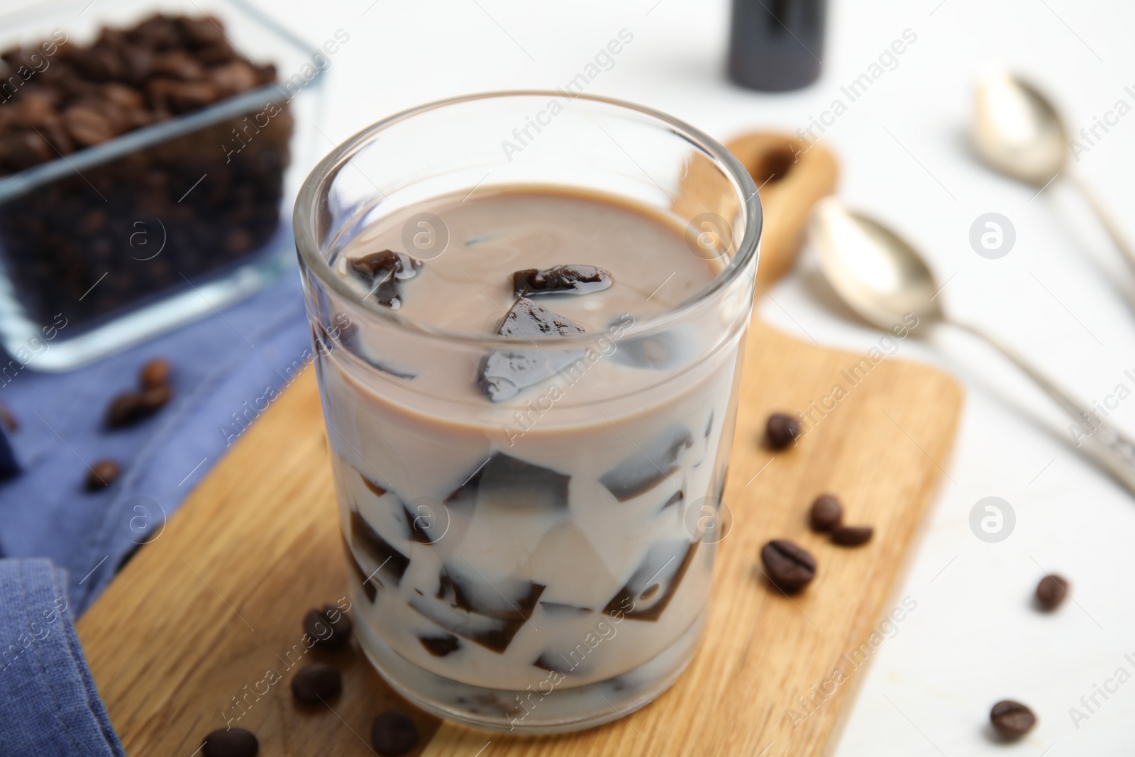 Photo of Glass of milk with grass jelly and coffee beans on white table, closeup