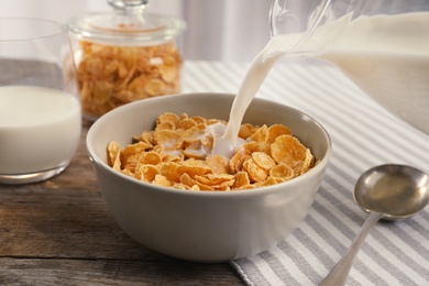 Photo of Pouring milk into bowl with healthy cornflakes on table