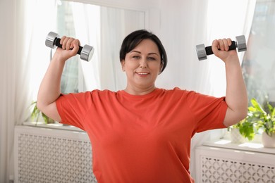 Photo of Overweight mature woman doing exercise with dumbbells at home