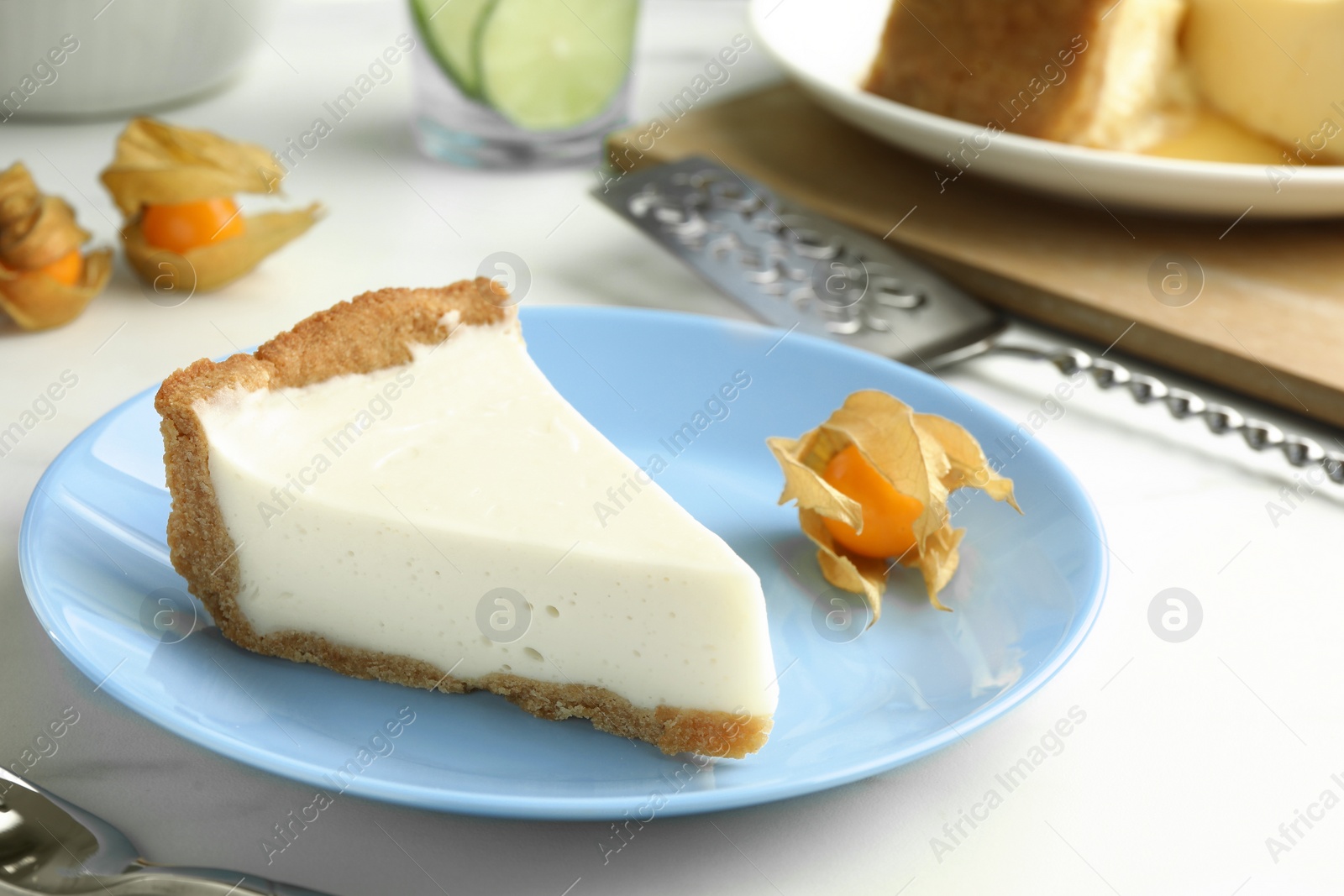 Photo of Piece of tasty vegan tofu cheesecake and physalis fruit on white table, closeup