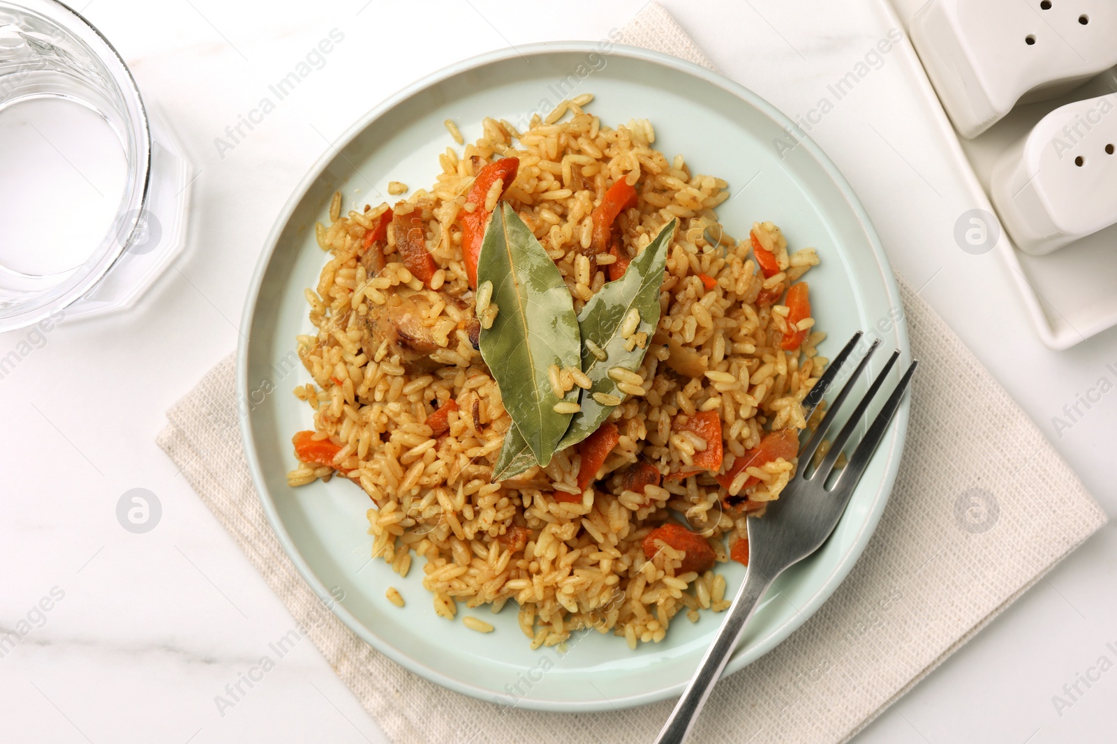 Photo of Delicious pilaf, bay leaves, fork and glass of water on white table, flat lay