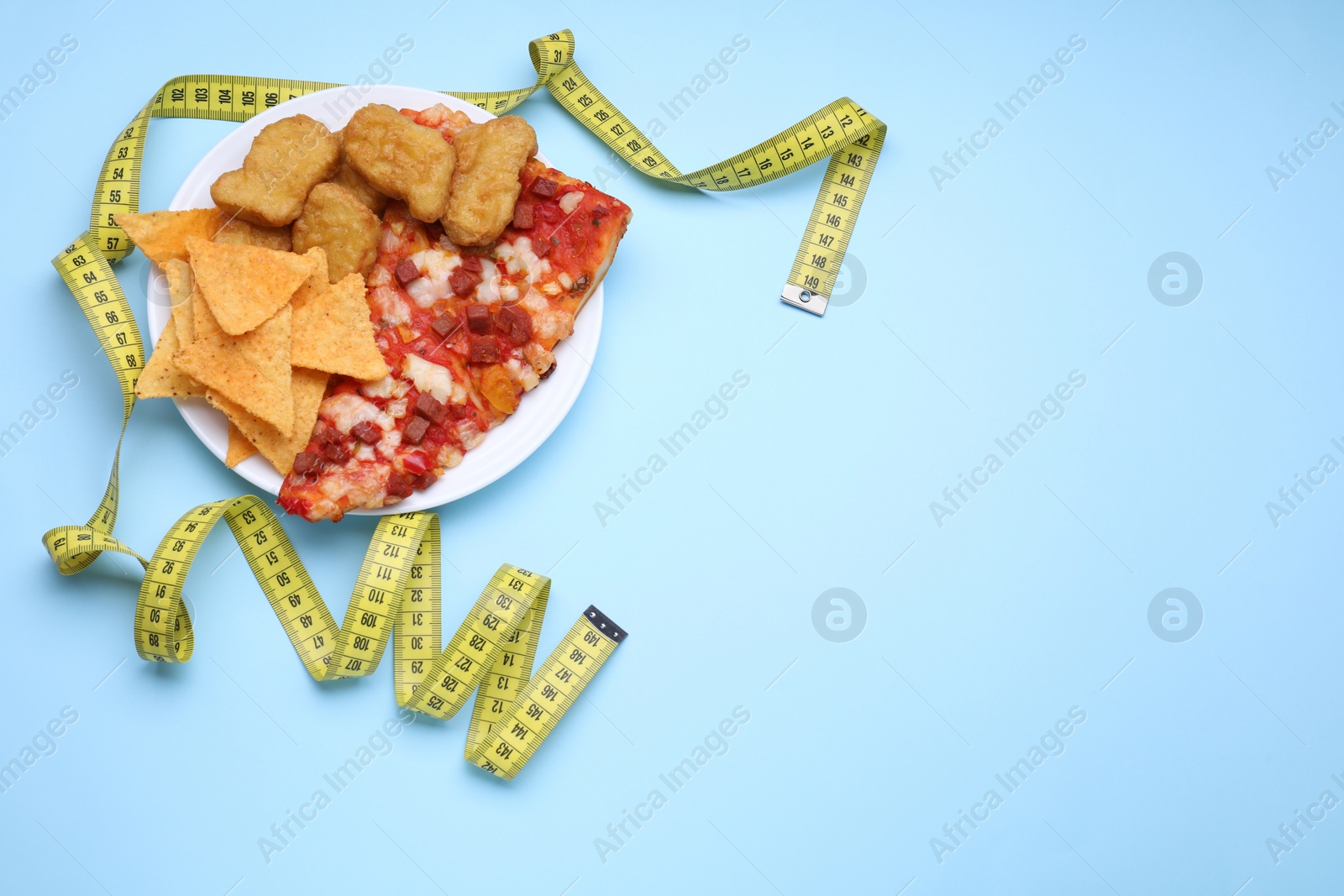 Photo of Chips, chicken nuggets, pizza and measuring tape on light blue background, flat lay and space for text. Diet concept