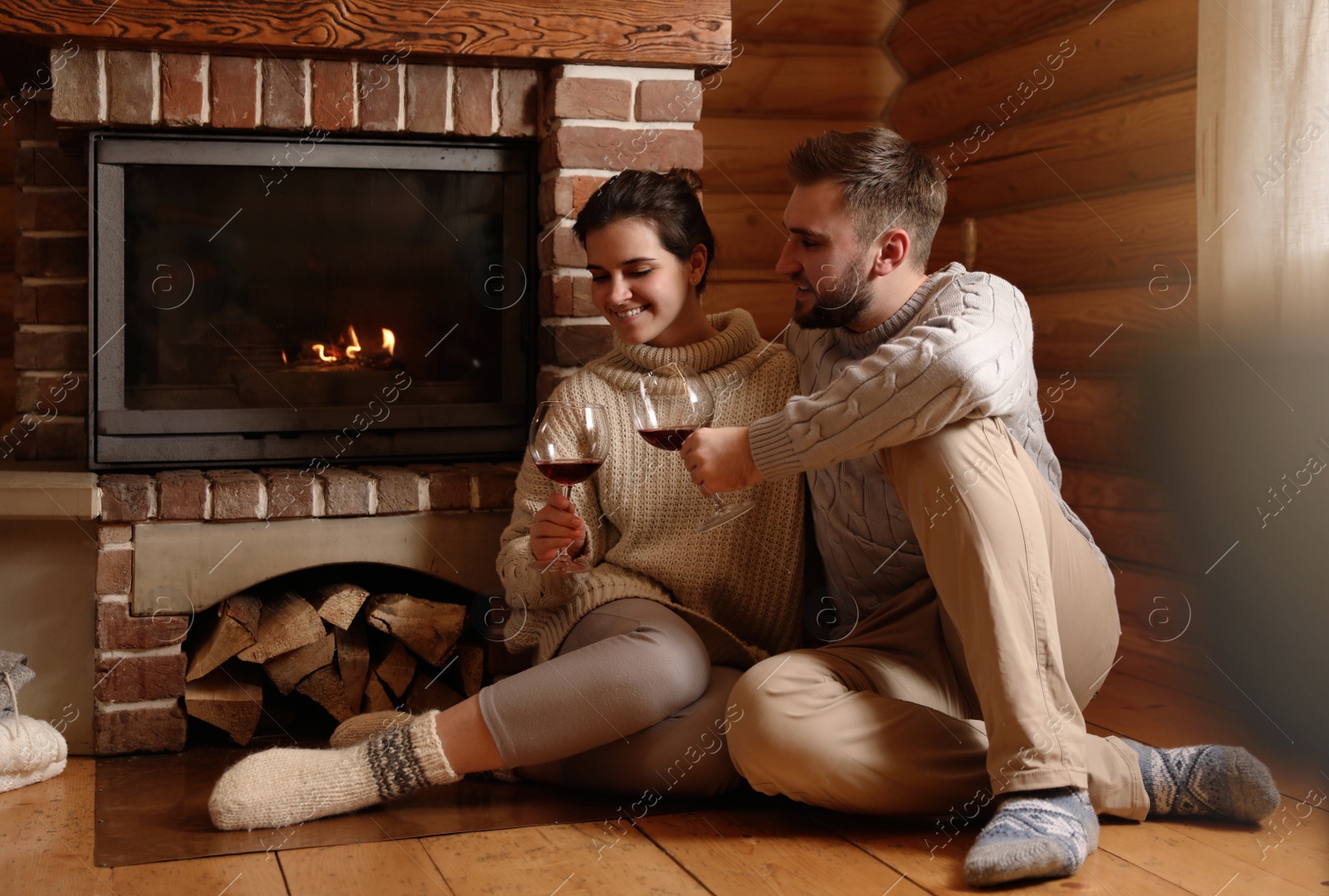 Photo of Lovely couple with glasses of wine near fireplace at home. Winter vacation