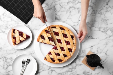 Woman cutting tasty cherry pie at white marble table, top view