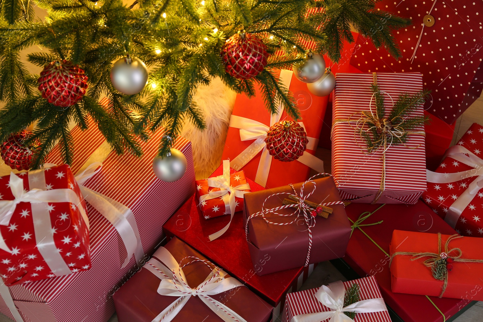 Photo of Pile of gift boxes near Christmas tree with fairy lights