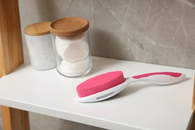 Photo of Pumice stone and jars on white shelf in bathroom