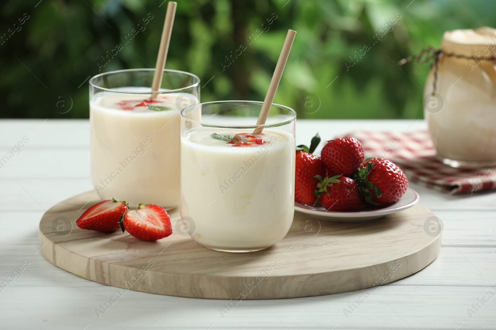 Photo of Tasty yogurt in glasses and strawberries on white wooden table outdoors