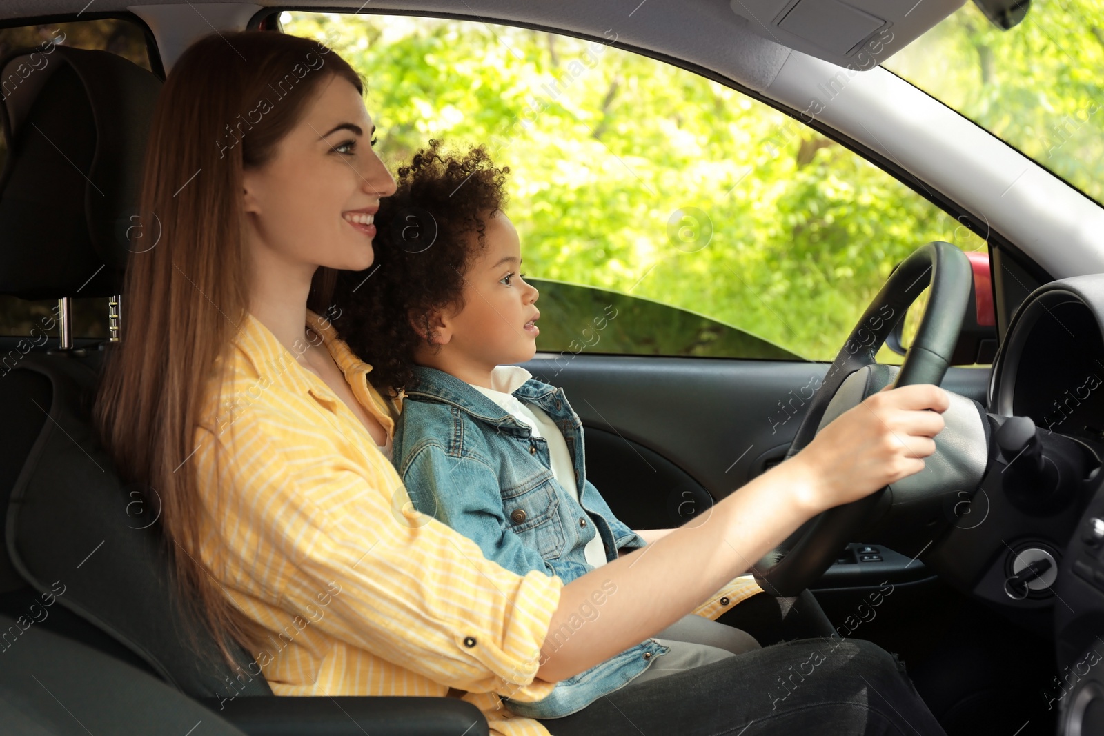 Photo of Mother with cute little daughter driving car together. Child in danger