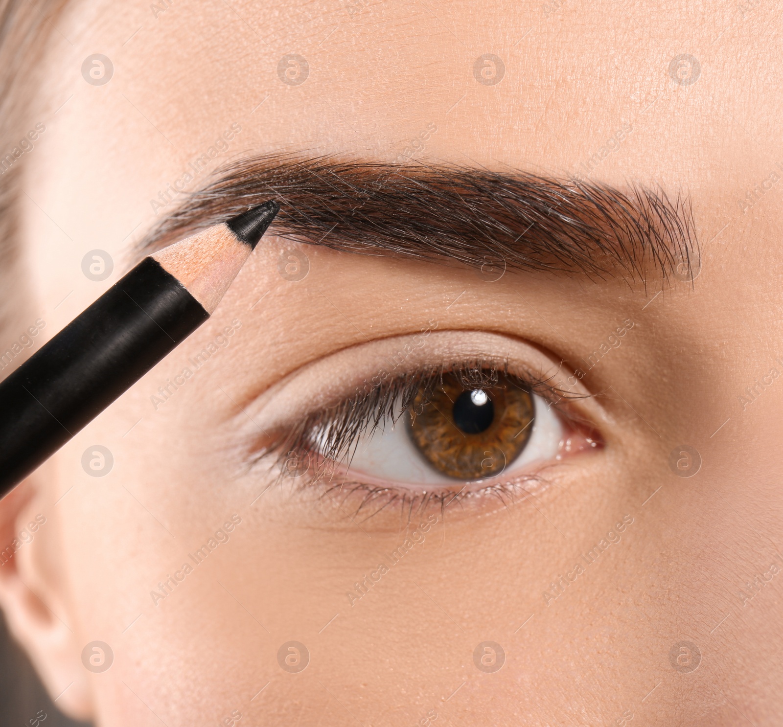 Photo of Young woman correcting eyebrow shape with pencil, closeup