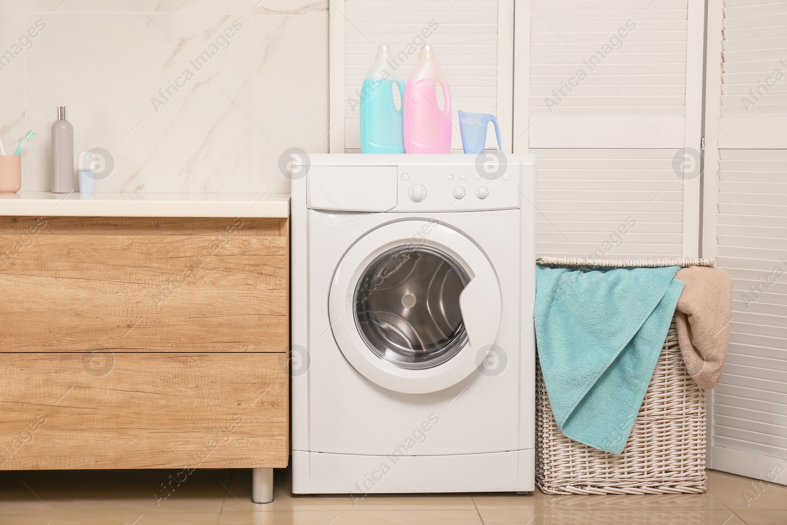 Photo of Wicker basket with laundry, detergents and washing machine in bathroom