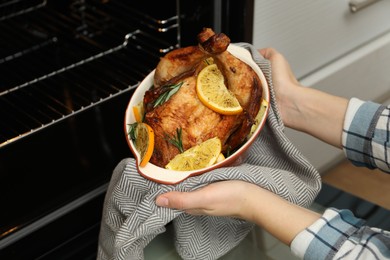 Photo of Woman taking baked chicken with orange slices out of oven, closeup