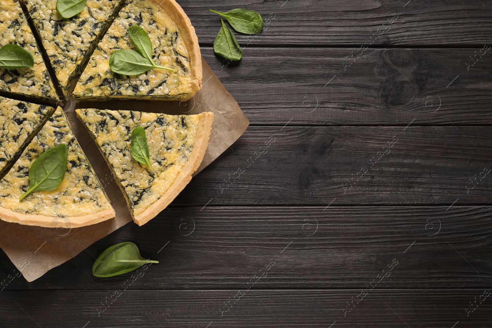 Photo of Sliced delicious homemade spinach pie on black wooden table, flat lay. Space for text