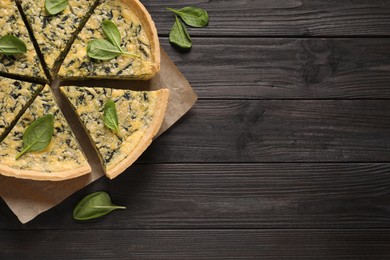 Sliced delicious homemade spinach pie on black wooden table, flat lay. Space for text