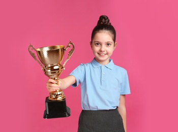 Photo of Happy girl in school uniform with golden winning cup on pink background. Space for text