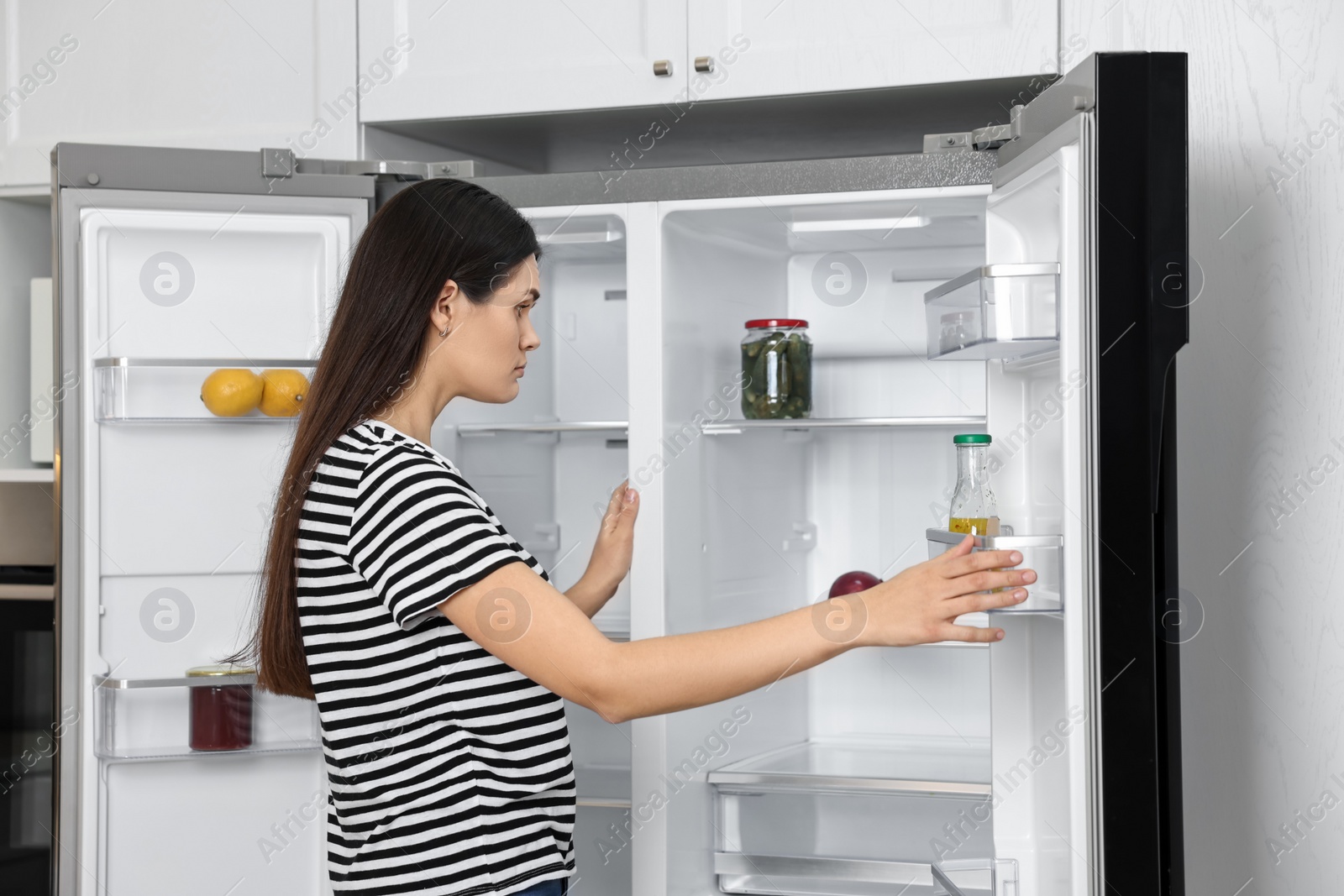 Photo of Upset woman near empty refrigerator in kitchen