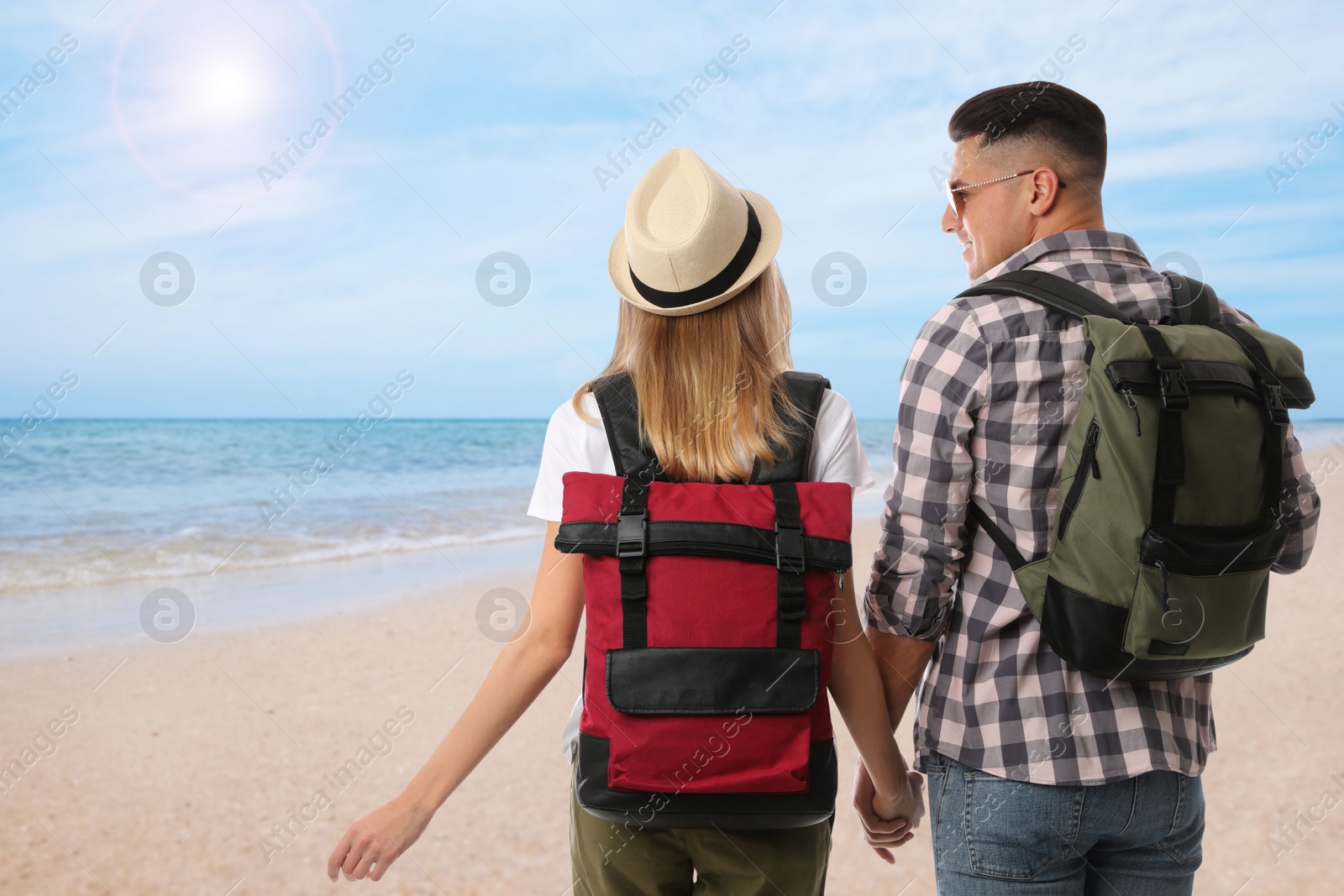 Image of Travelers with backpacks on sandy beach near sea during summer vacation trip, back view. Space for text