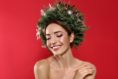 Beautiful young woman wearing Christmas wreath on red background