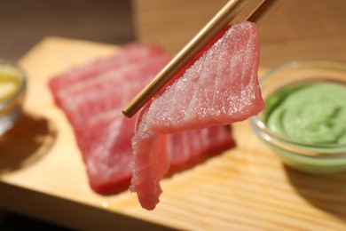 Holding tasty sashimi (piece of fresh raw tuna) with chopsticks against blurred background, closeup