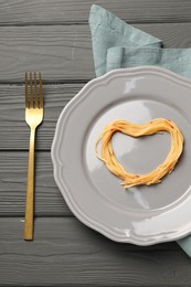 Photo of Heart made with spaghetti and fork on grey wooden table, top view