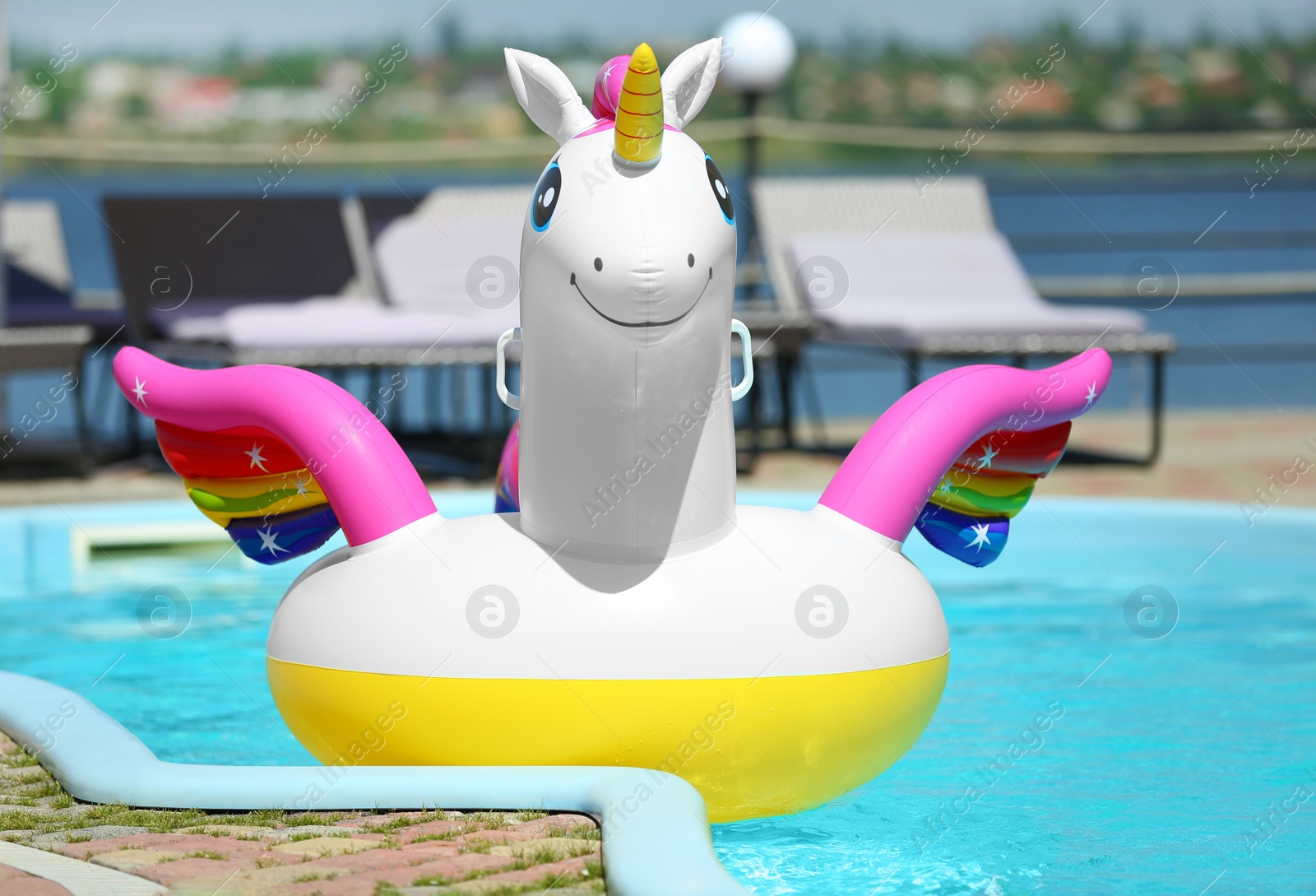 Photo of Funny inflatable unicorn ring floating in swimming pool on sunny day, outdoors