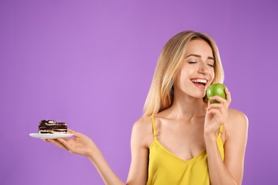 Photo of Woman choosing between cake and healthy apple on violet background