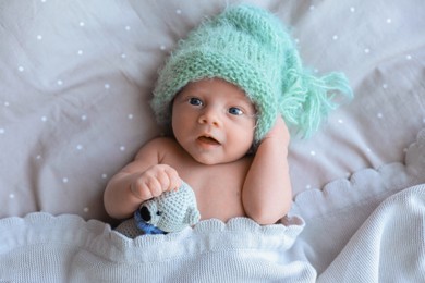 Cute newborn baby in warm hat with toy lying on bed, top view