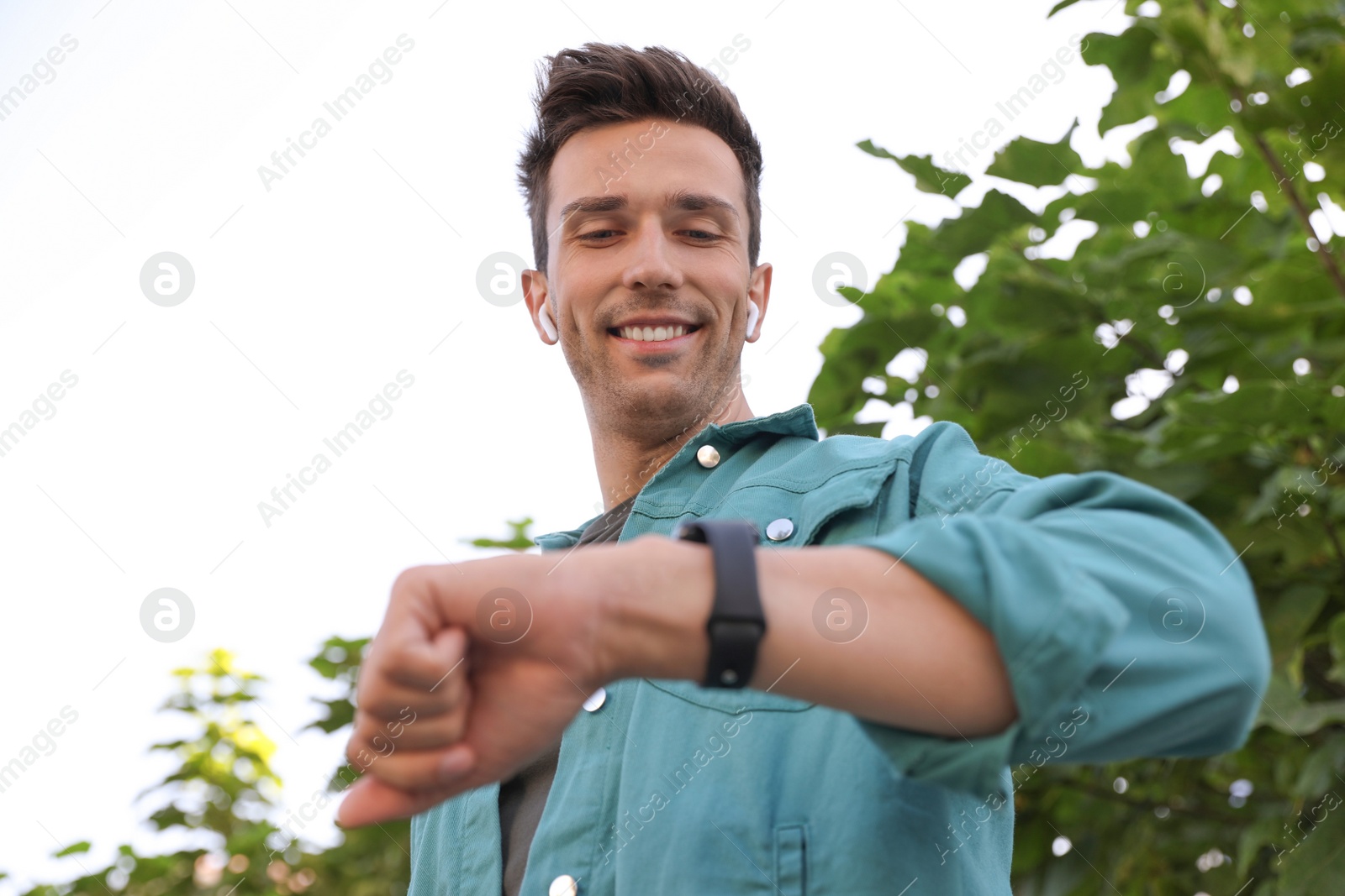 Photo of Young man with wireless earphones and smart watch in park