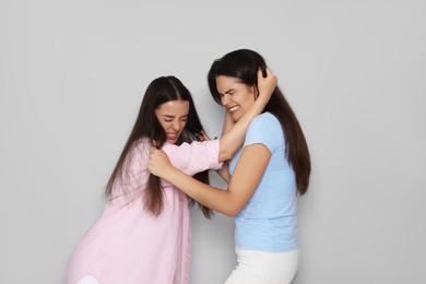 Aggressive young women fighting on light grey background