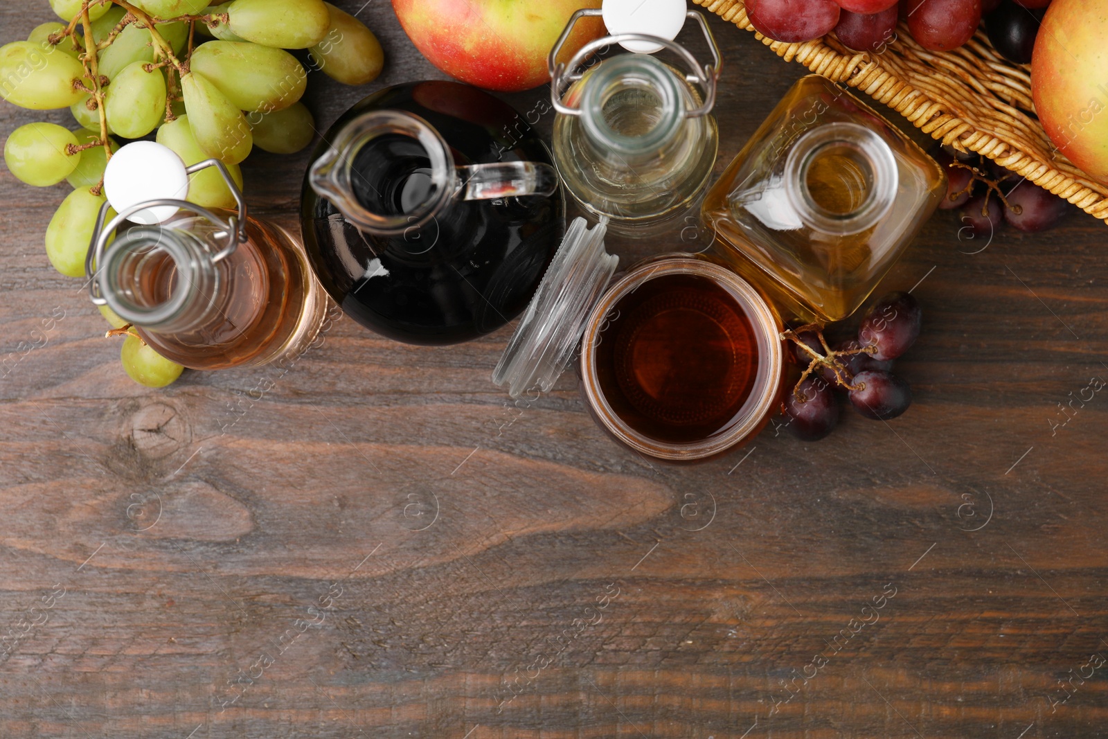 Photo of Different types of vinegar and fresh fruits on wooden table, flat lay. Space for text