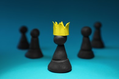 Photo of Black plasticine chess pieces and one with paper crown on light blue background