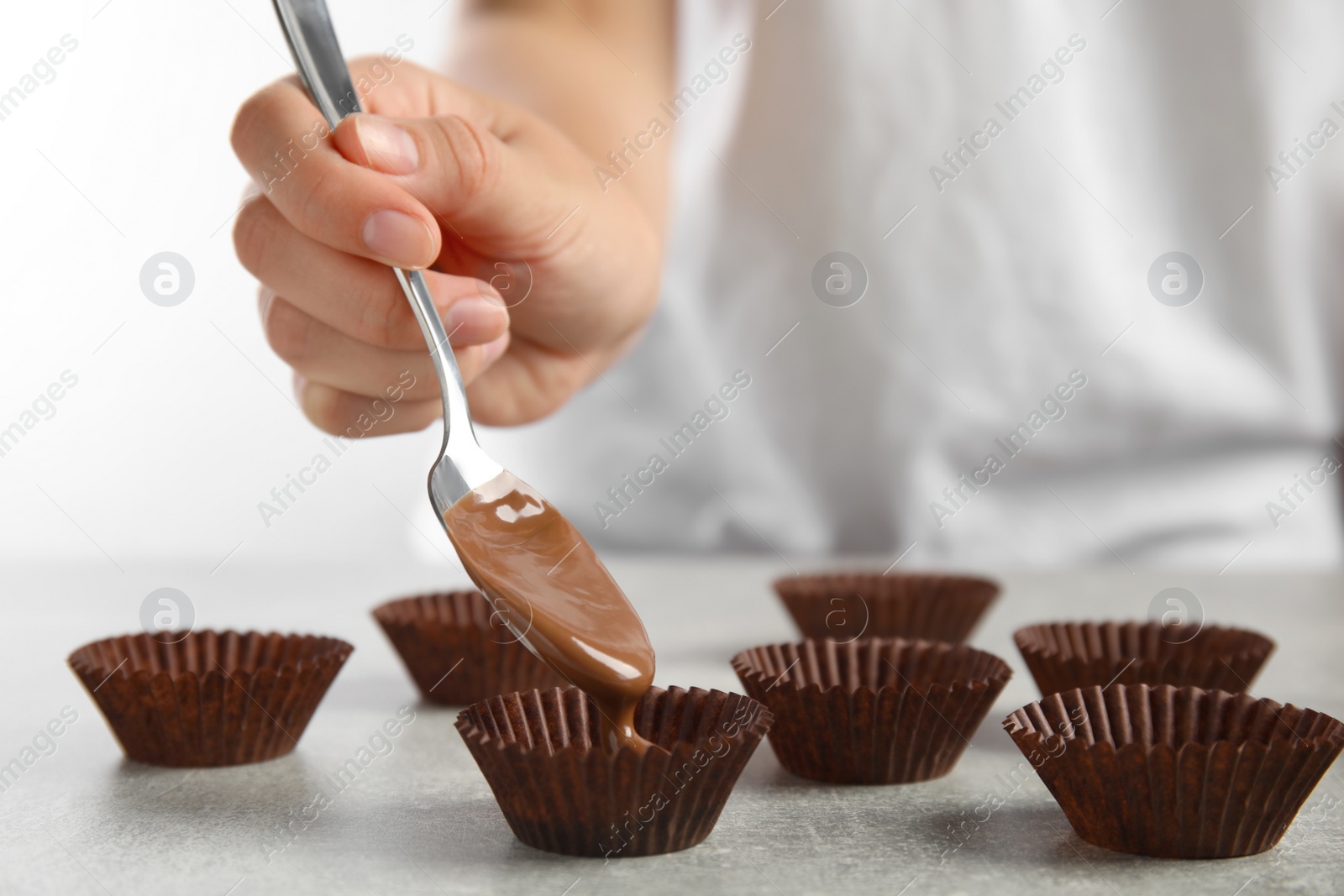 Photo of Professional confectioner making delicious chocolate candies at grey table, closeup