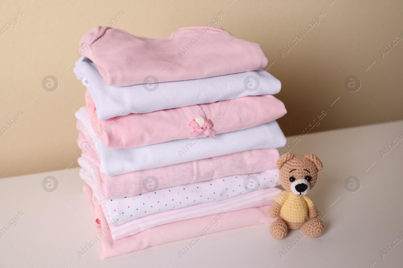 Photo of Stack of baby girl's clothes and toy bear on white table