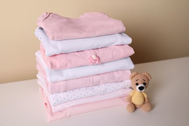 Photo of Stack of baby girl's clothes and toy bear on white table