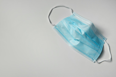 Photo of Disposable face mask on light background, top view with space for text. Protective measures during coronavirus quarantine