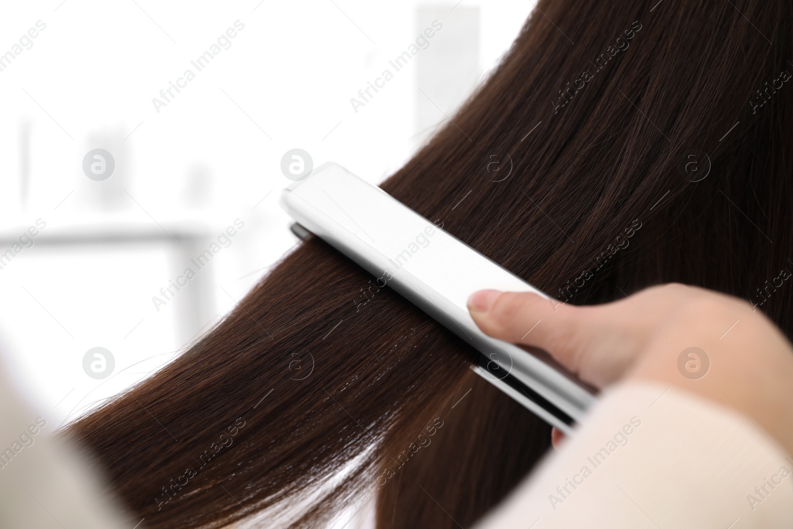 Photo of Hairdresser using modern flat iron to style client's hair in salon, closeup