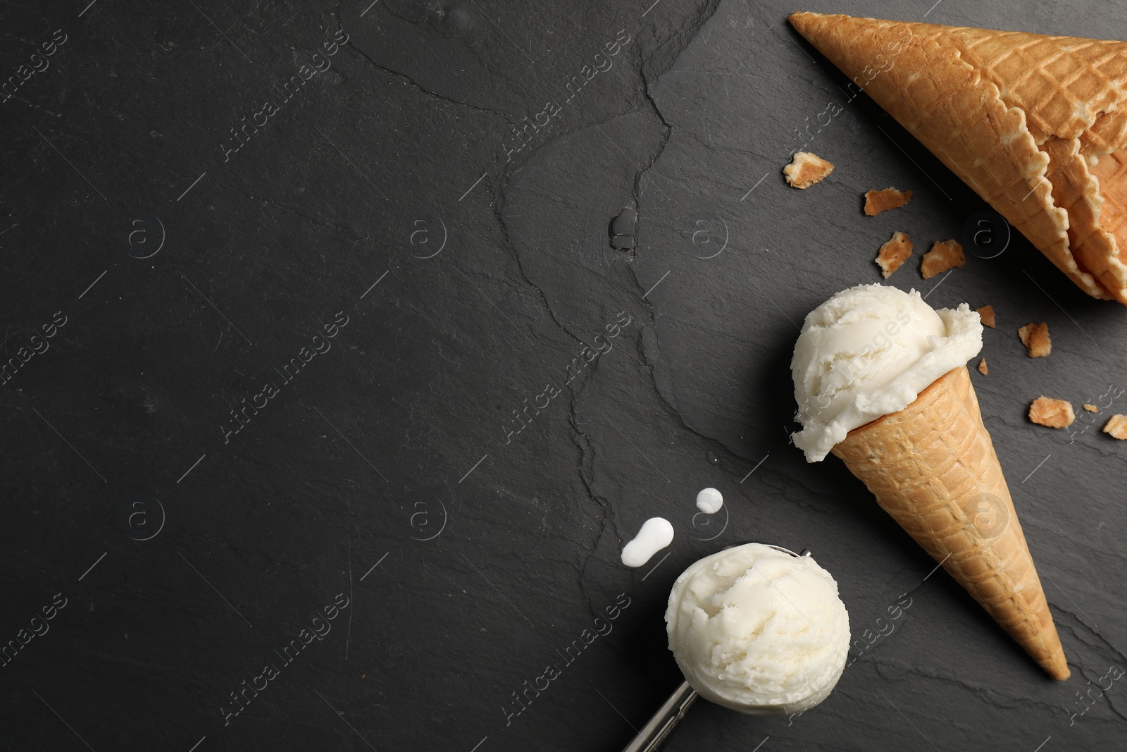 Photo of Ice cream scoops in wafer cones on dark gray textured table, flat lay. Space for text
