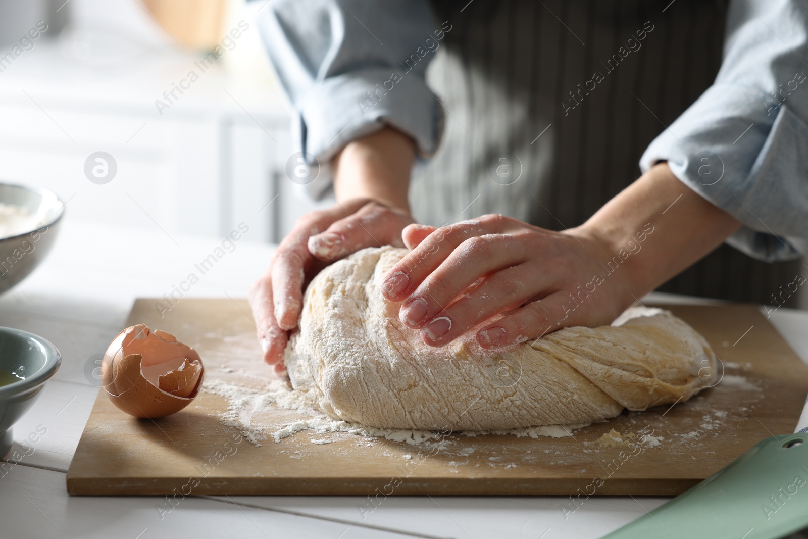 Photo of Woman kneading dough at white wooden table in kitchen, closeup