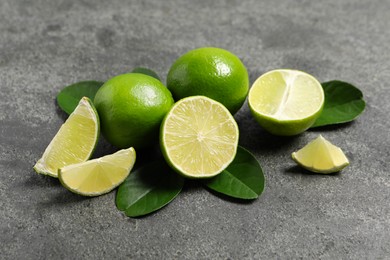 Photo of Fresh ripe limes and leaves on grey table, closeup