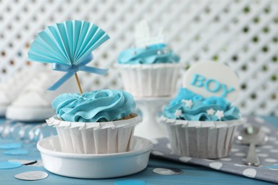 Delicious cupcakes with light blue cream and toppers for baby shower on table