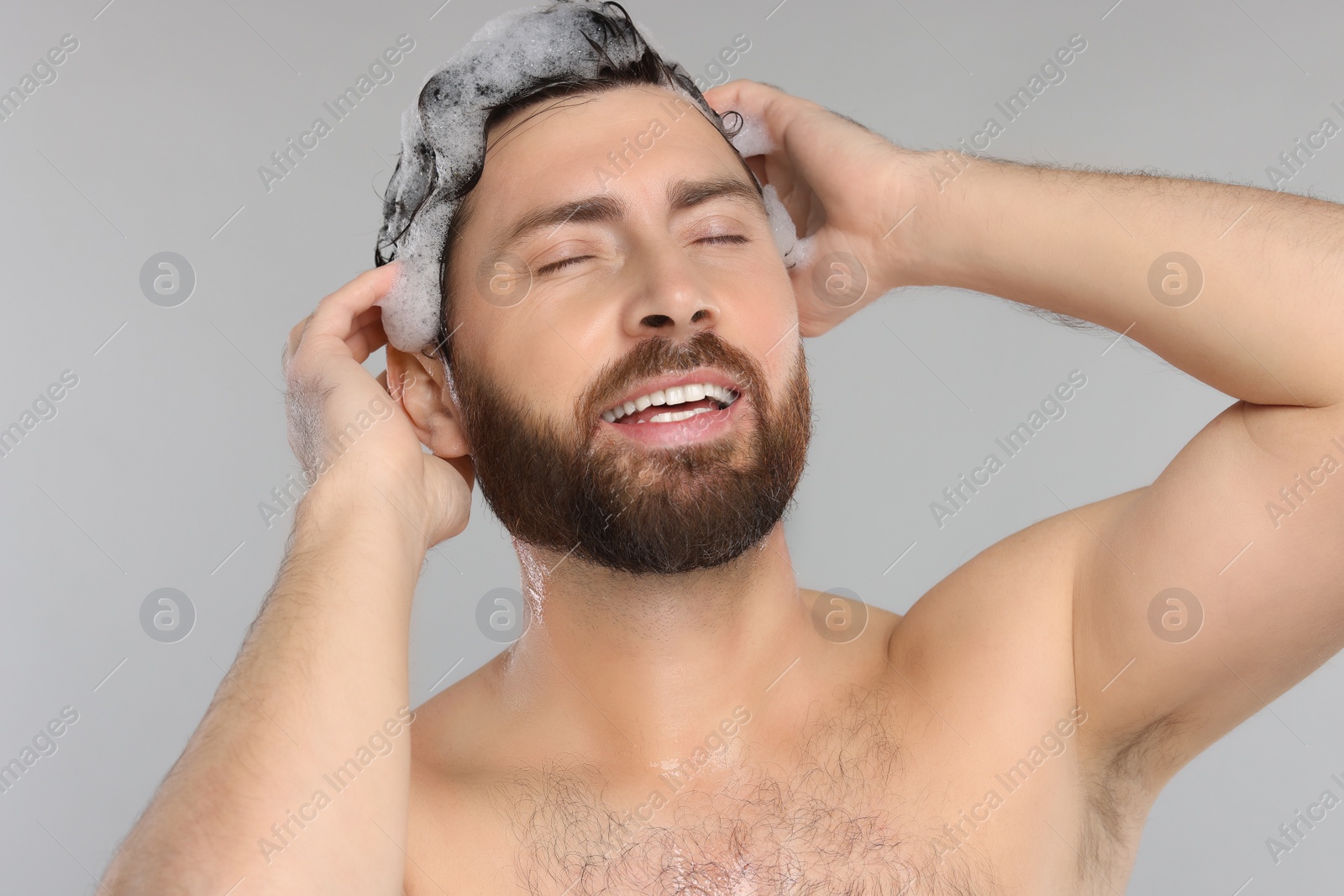 Photo of Happy man washing his hair with shampoo on grey background, closeup
