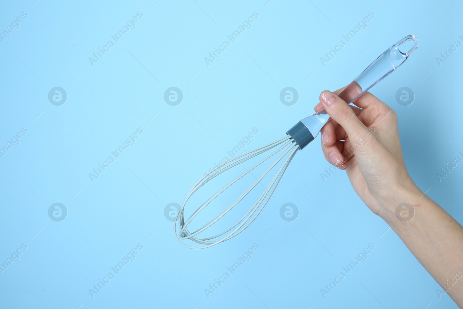 Photo of Woman holding whisk on light blue background, closeup. Space for text