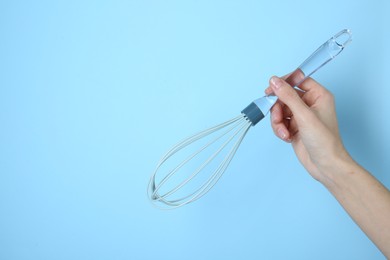 Photo of Woman holding whisk on light blue background, closeup. Space for text