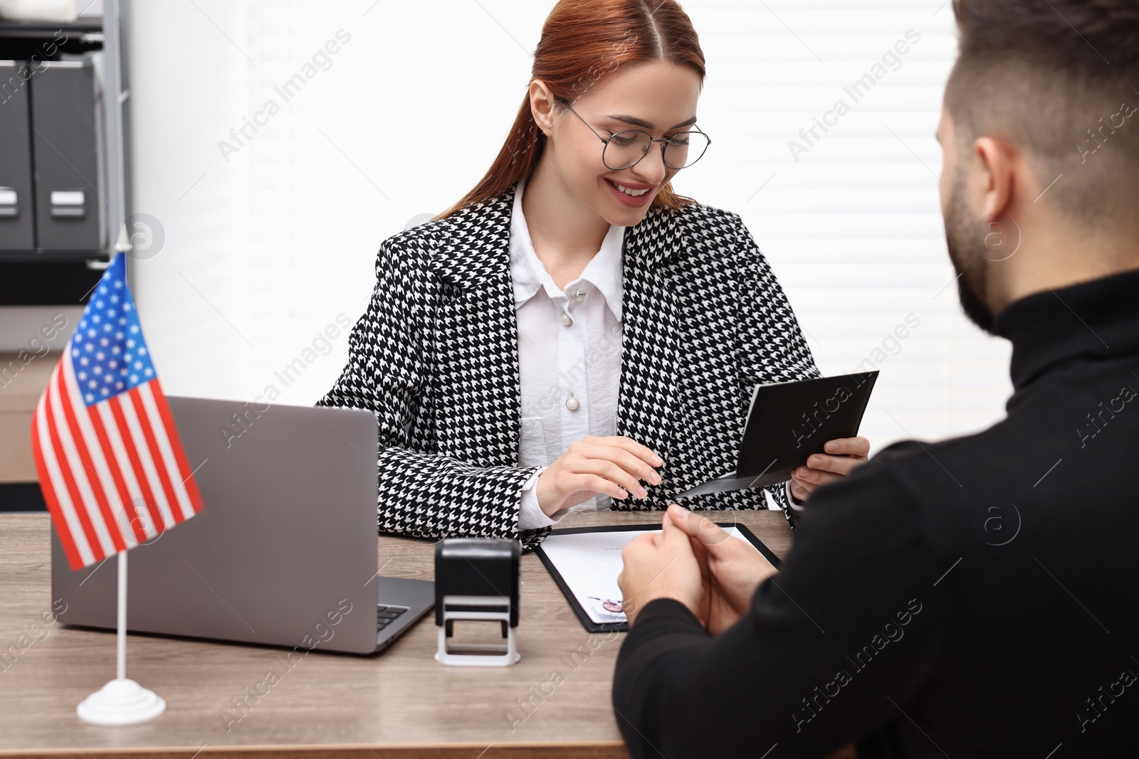 Photo of Immigration to United States of America. Smiling embassy worker checking man's documents in office