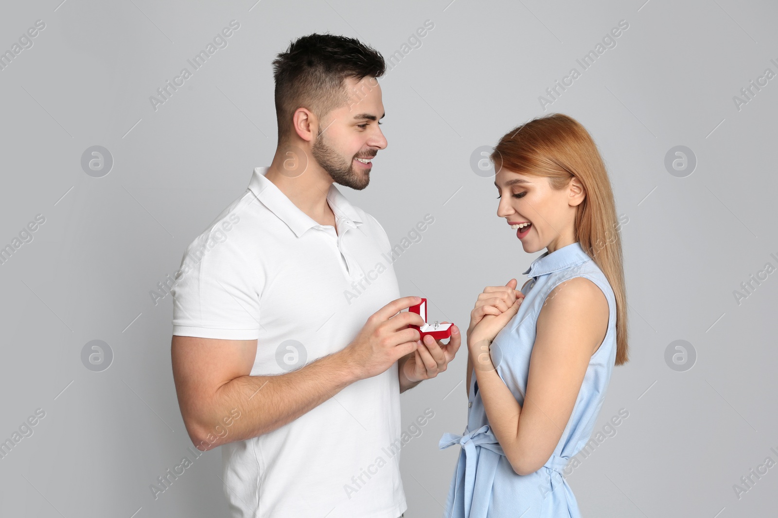 Photo of Man with engagement ring making marriage proposal to girlfriend on light grey background