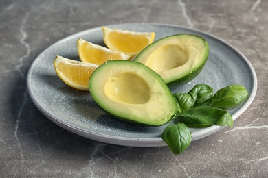 Plate with ripe avocado, basil and lemon on grey background