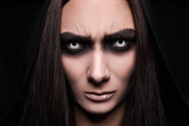 Photo of Mysterious witch with spooky eyes on black background, closeup