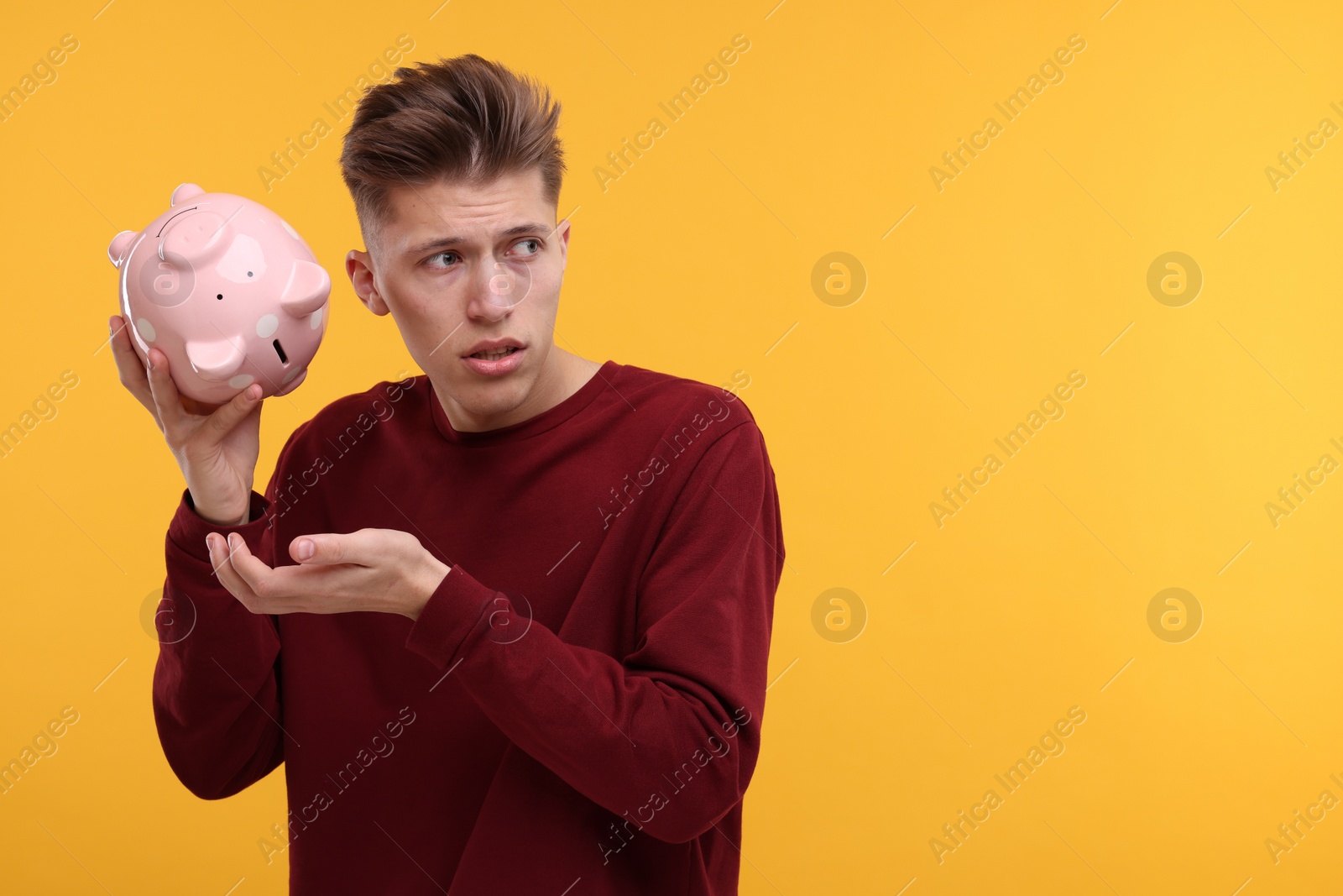 Photo of Upset man with empty piggy bank on yellow background. Space for text